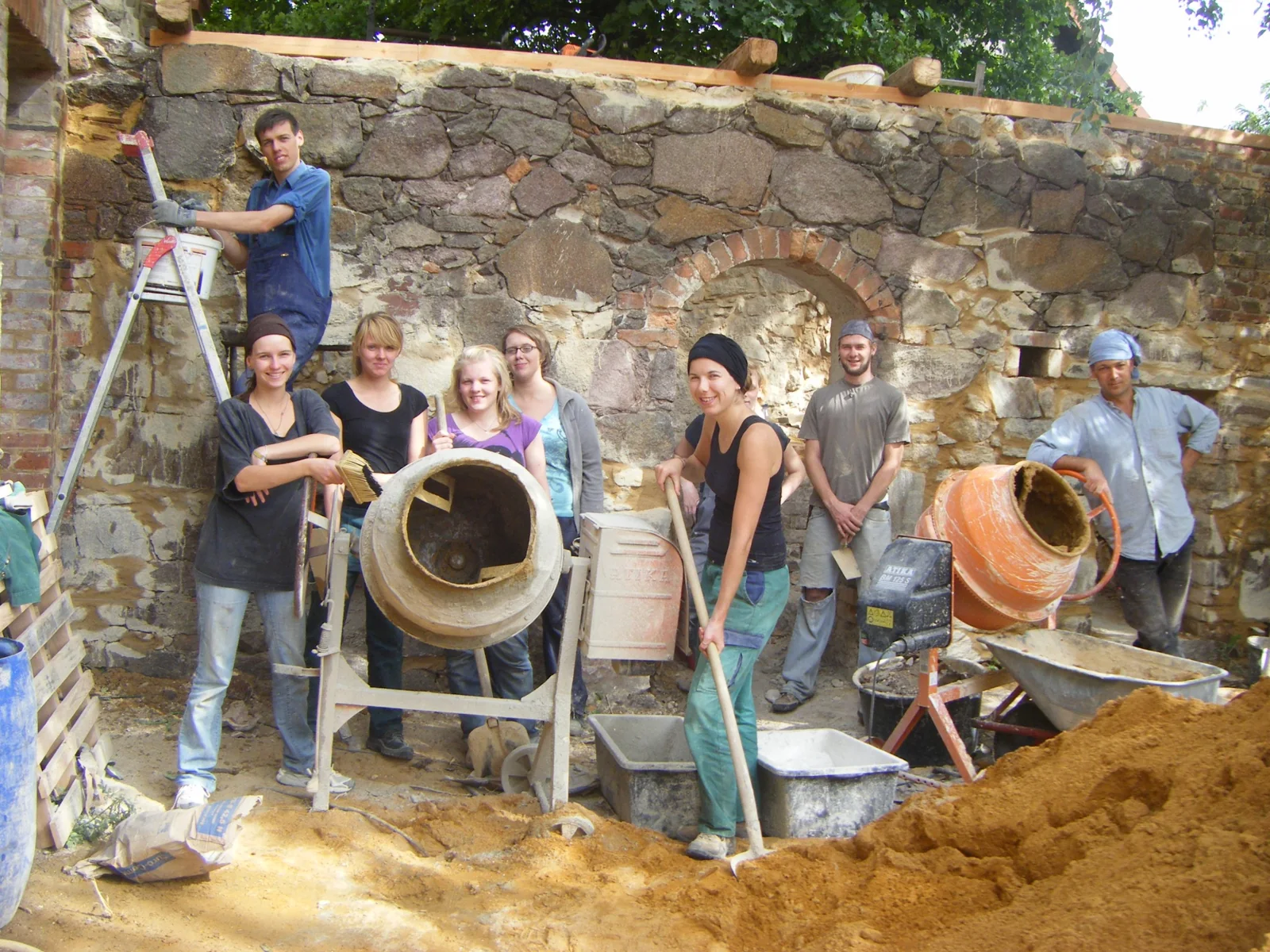 Menschen bauen gemeinsam mit Werkzeug und Mörtel an einer Mauer