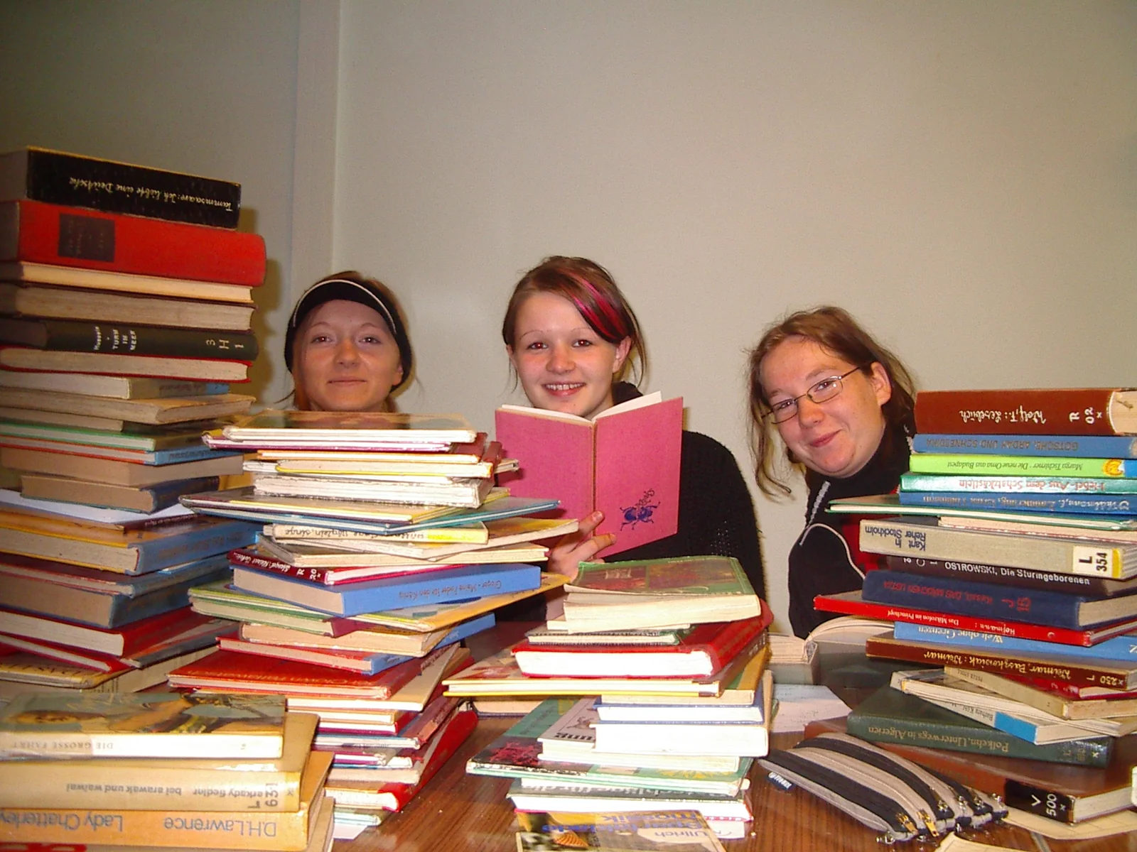 Drei junge Frauen zwischen Bücherstapeln mit einem aufgeschlagenen Buch