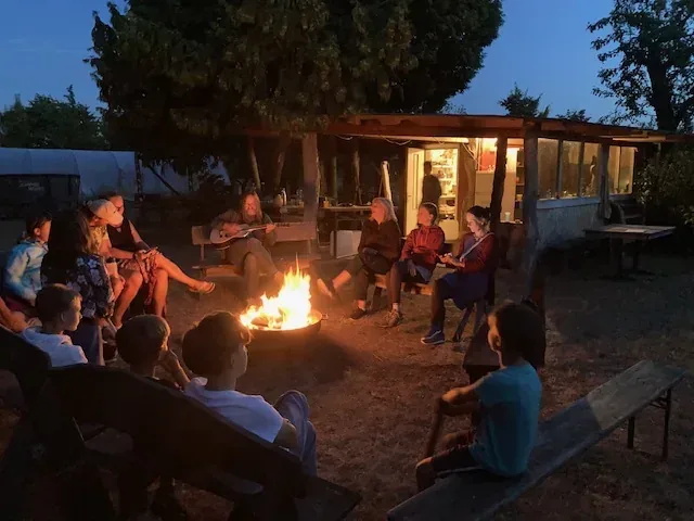Eine Gruppe sitzt am Lagerfeuer, Warthy begleitet die Gitarrenrunde